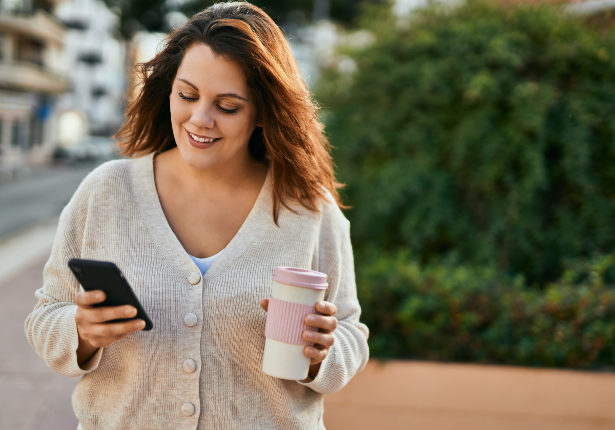Woman holding coffee and looking at phone in Ireland